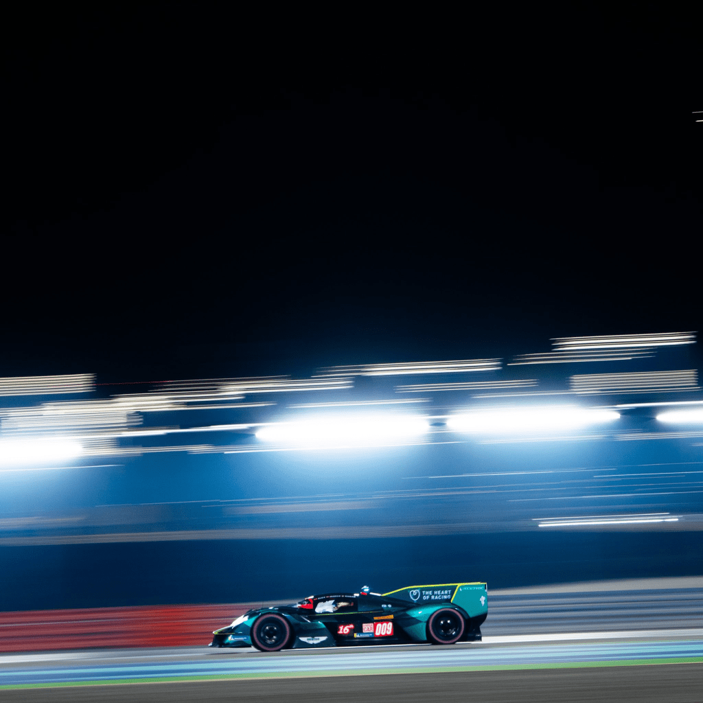 Aston Martin's #009 Valkyrie Hypercar at speed under the lights in Qatar, shown in a panning shot so all the lights are elongated.